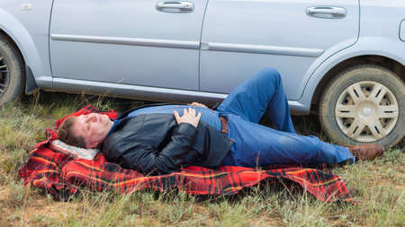 The tired driver lies on a blanket near the car.の写真素材
