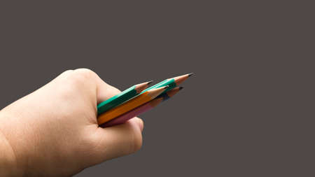 A man's hand holds a bunch of colored pencils on a gray background.