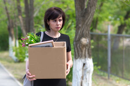 A frustrated fired woman with a box in her hands walks through the city.