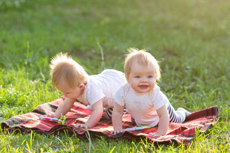 Little twin girls in the city park in the summer crawl on a blanket.の写真素材