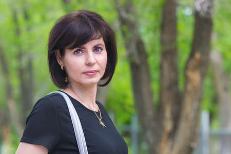 Portrait of a brunette woman in a black dress on a walk in a city park.の写真素材