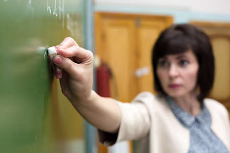 A teacher writes a solution to math problem with chalk on a blackboard.