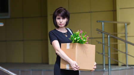 Fired accountant of 40 years with box of personal belongings leaves work.の写真素材