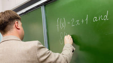 A male school math teacher at the blackboard explains solution of the problem.
