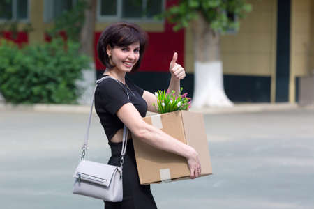 A happy brunette woman with a box of personal belongings shows with a hand gesture that she was hired.の写真素材