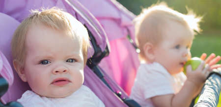 Portrait of Caucasian twin children of 6 months of age with blonde hair sitting in baby carriage.