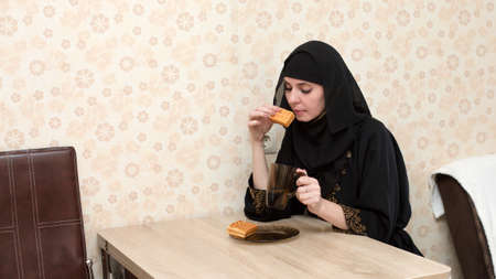 A Muslim woman in national clothes having breakfast at the table in her apartment.の写真素材