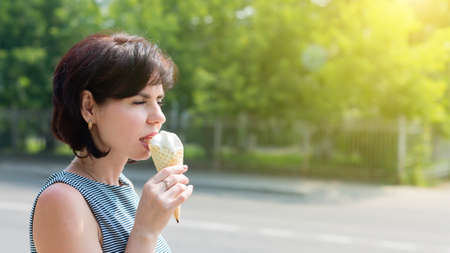 Smiling positive brunette with ice cream in her hand on the street of the city, copy spaceの写真素材