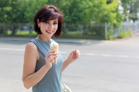 Smiling positive brunette with ice cream in her hand on the city street.の写真素材