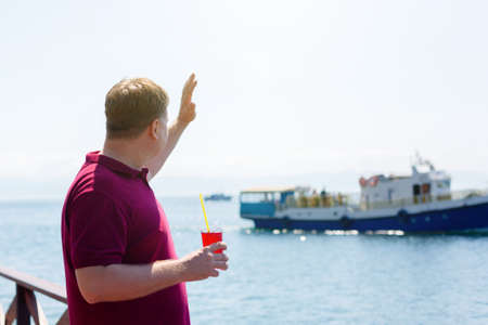A man on a pier by the sea with smile waves to a passing ship.の写真素材