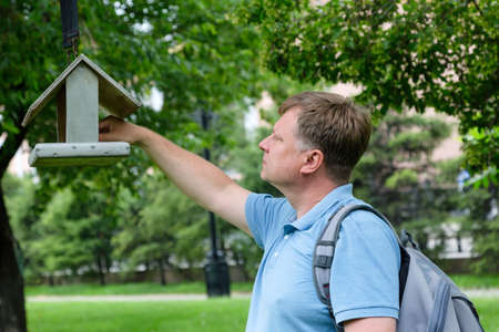 An adult tall blond man pours bird food into the feeder.の写真素材