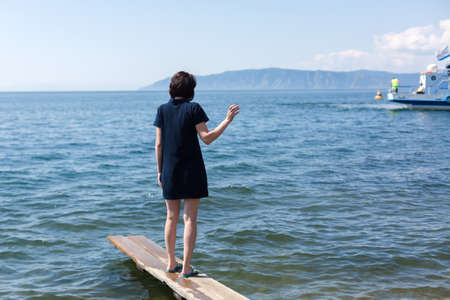 woman with sadness on the pier sees off her beloved sailing away on ship waving her hand after him.の写真素材