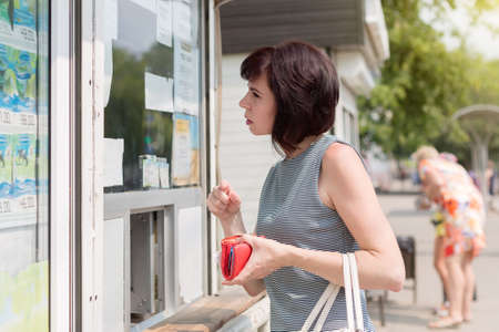 A brunette on the street with a red wallet in her hand is buying ice cream at a kiosk.の写真素材