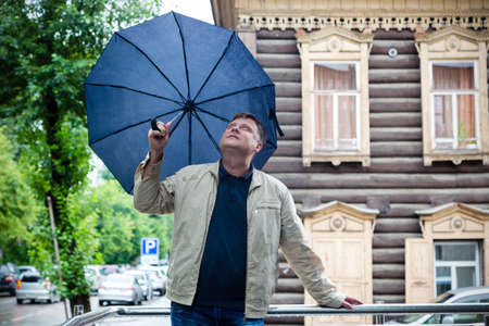 A 40-45-year-old man in a white jacket with an umbrella in his hands enjoys the autumn weather.の写真素材