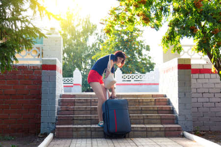 A woman with heavy suitcase hardly climbs the stairs of railway station.の写真素材