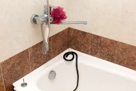 A black venomous snake on the edge of a white bathtub in an apartment.