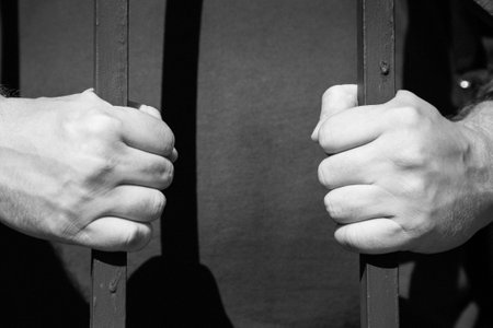 Strong male hands clenched into a fist hold a metal grate. Black and white