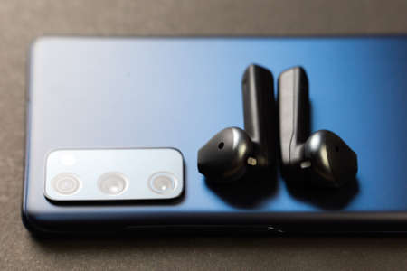 A new smartphone with wireless headphones on gray background, Close-up.の写真素材