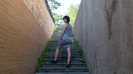 slender brunette climbs the stairs in narrow dangerous deserted dark alley.の写真素材