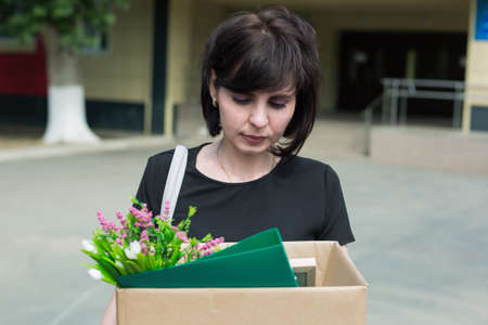 Upset brunette ecomist with a box personal belongings leaves work after being fired.