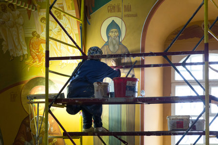 Irkutsk, Russia - July 31, 2021, A woman artist restores a wall icon in a temple. Editorial