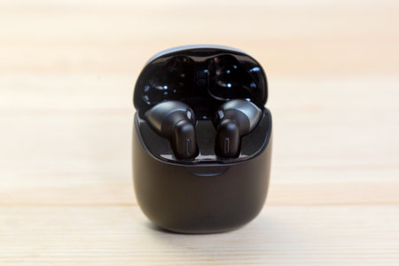Wireless headphones are charged in a container box. Wood background