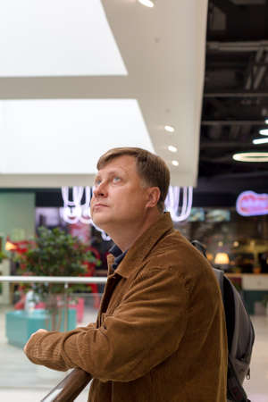 An adult blond man in a corduroy jacket is bored at the mall, waiting for his wife.の写真素材