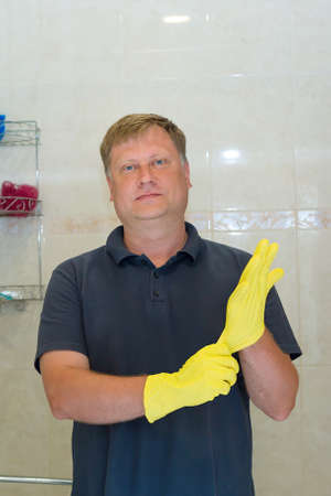 A man puts rubber gloves on his hand for cleaning bathroom.の写真素材