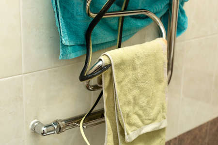 A black venomous snake curled up ball is warming itself on a radiator with a towel in the bathroom.の写真素材