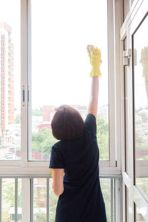 small woman with difficulty washes high windows on the balcony.の写真素材