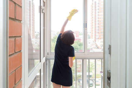 A small woman with difficulty washes the high windows on the balcony.