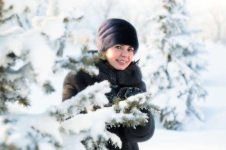 A 35-40-year-old woman with smile looks out from behind the fluffy branches spruce covered with snow.の写真素材