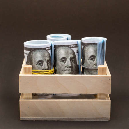 Bundles of dollars wrapped with an elastic band in a wooden box on a black background.の写真素材