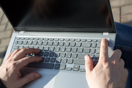 Male hands laptop keyboard typing text, the concept of a freelancer's work in the fresh air.