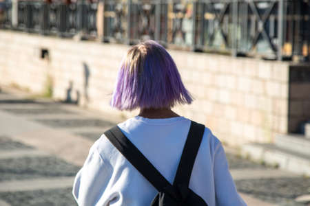 A young girl with purple hair color walks down the street of the city.の写真素材