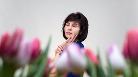 Portrait of a dreaming woman with her eyes closed against a background of beautiful fresh tulips.の写真素材