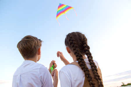 A girl and a boy launch a bright kite into the sky, a view from the back.の写真素材