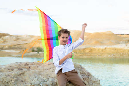 A boy with a kite in his hand sits a stone near the water.の写真素材