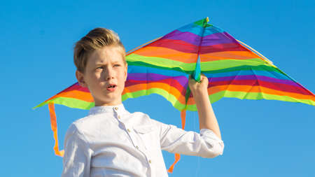 A handsome boy in white shirt with a multicolored kite on a blue sky background.
