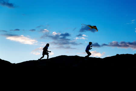 Children run with a kite at sunset, beautiful silhouettes.の写真素材