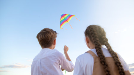 A girl and a boy launch bright kite into the sky, a view from the back.の写真素材
