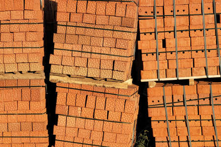 Brown bricks stacked on pallets along construction site fence.