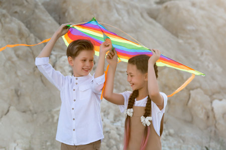 A girl and a boy carry a bright colored kite over their heads while walking in the mountains.の写真素材