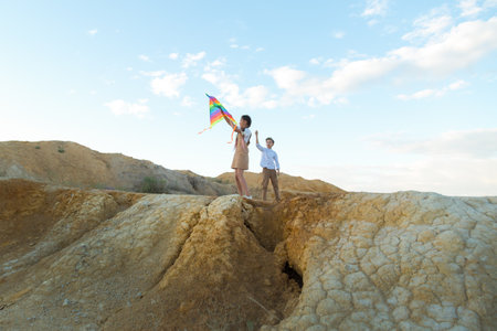 Brother and sister launch bright big kite into the sky near a flowing river.の写真素材