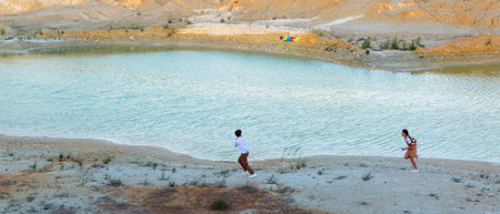 A boy and girl with a kite are running through a mountainous area along a river.