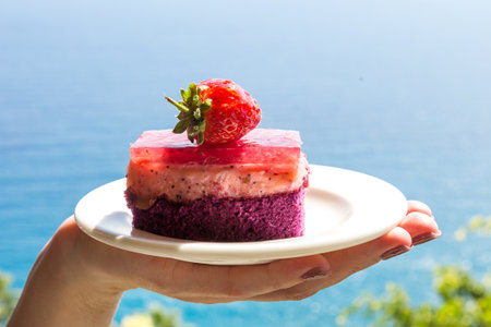 Strawberry cake in a plate in female hands against the backdrop of the sea. Decorating cakes with whole berries.の写真素材