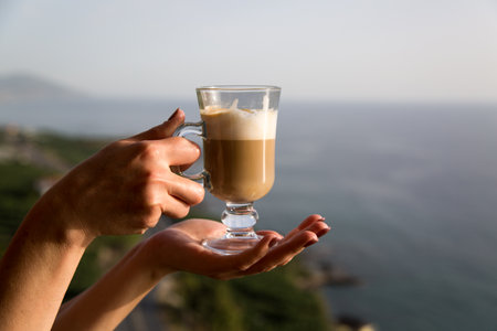Glass mug with coffee at sunset in female hands. close-up.