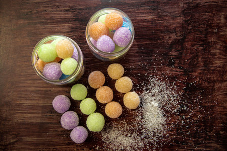 Colored round candy balls sprinkled with sugar in a glass jar and a wooden table.の写真素材