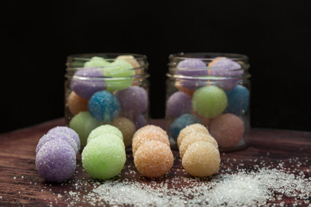 Colored round candy balls sprinkled with sugar in a glass jar and on wooden table.の写真素材