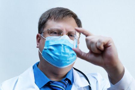 Male doctor looks ampoule with medicine vaccine, close-up white background.の写真素材